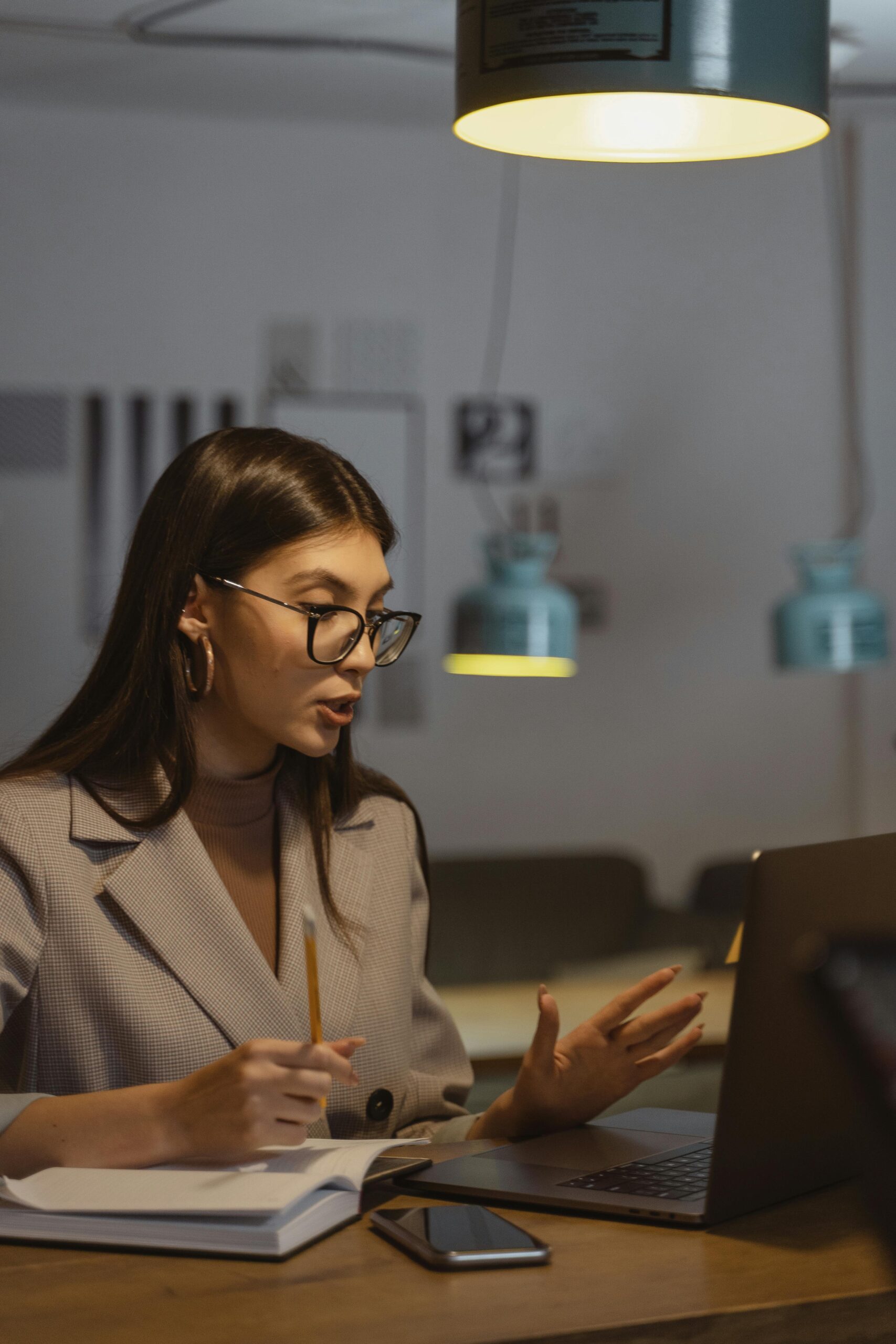 pexels-photo-5685961-5685961 A young businesswoman working late at her desk, engaged in an online meeting with a laptop, notebook, and smartphone.